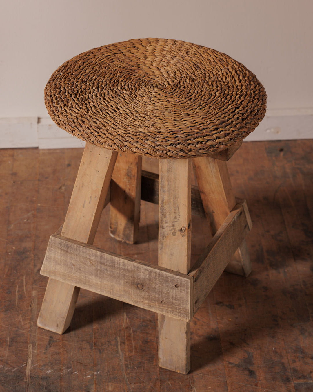 A rustic stool with a round woven seat and a light wooden base.