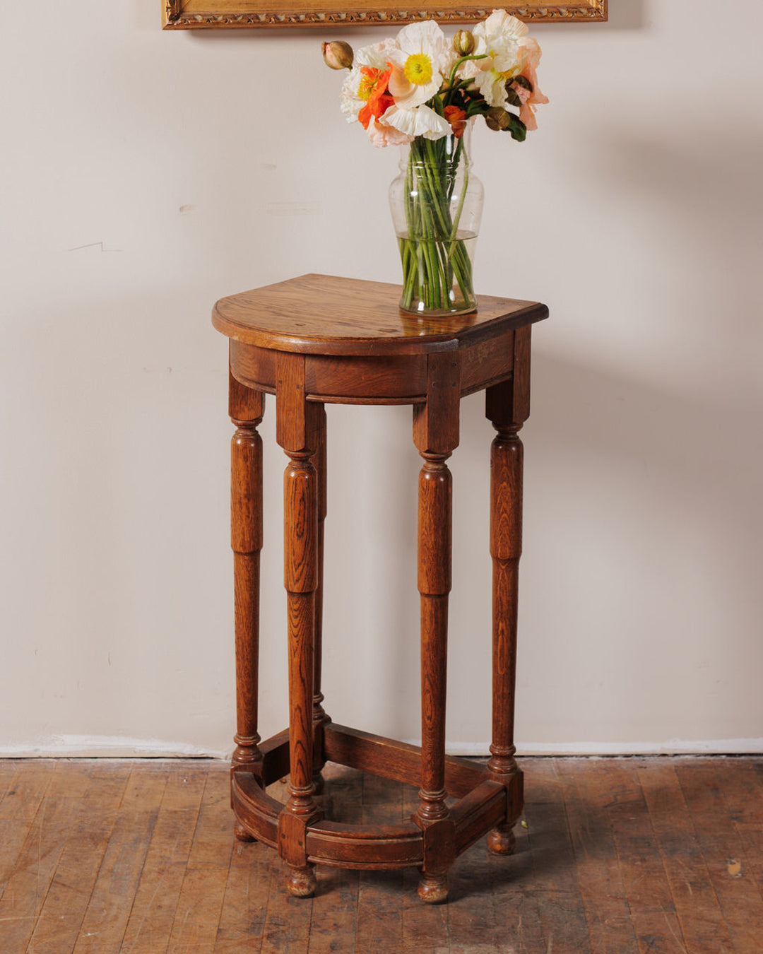 A wooden corner table with a vase of white and orange poppies.