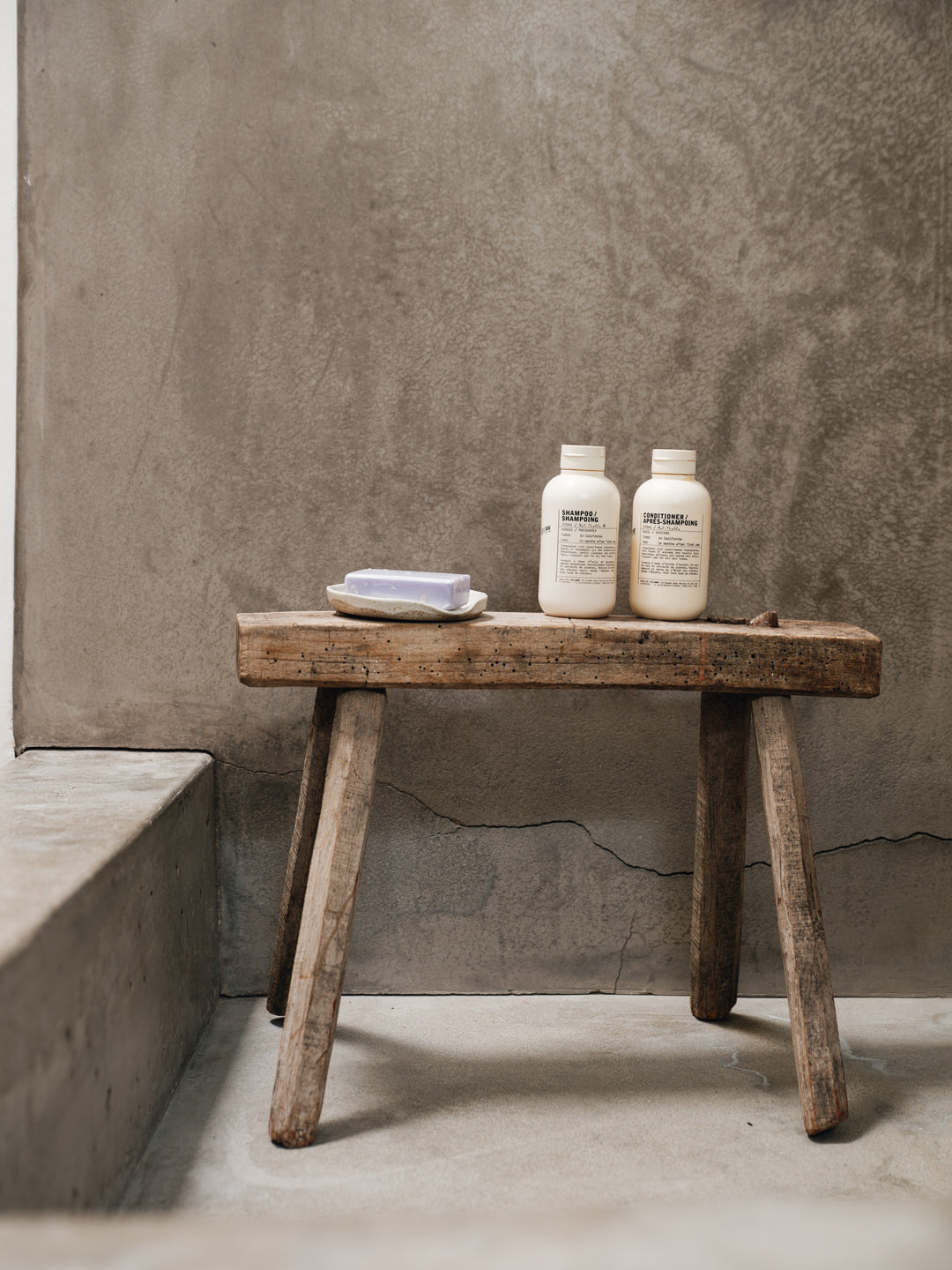 two bottles of essential shampoo and conditioner sit on a wooden bench