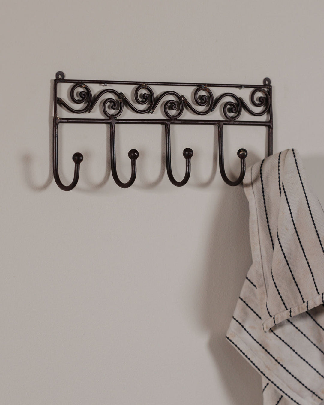 Decorative dark metal rack with five hooks on a light wall, one hook holding a white striped towel.
