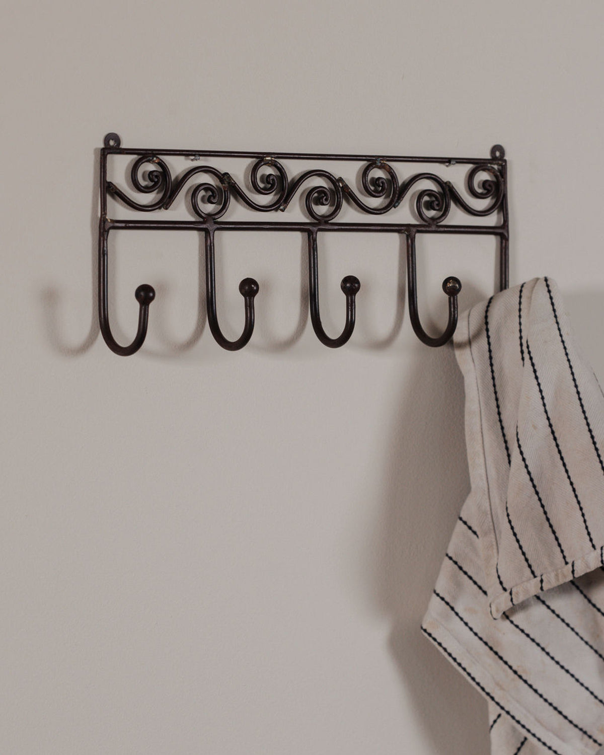 Decorative dark metal rack with five hooks on a light wall, one hook holding a white striped towel.