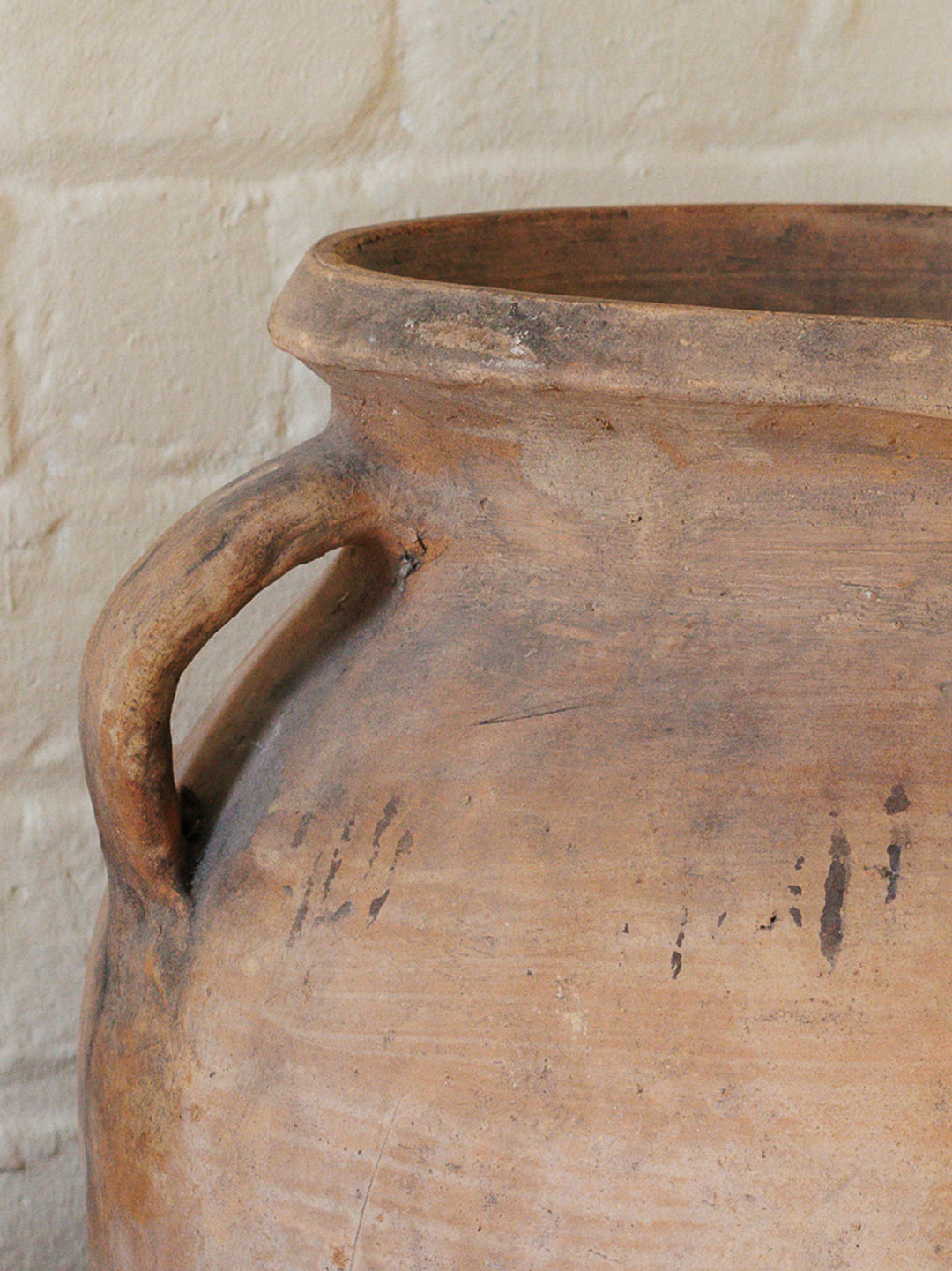 a large clay pot with a handle is against a white brick wall .