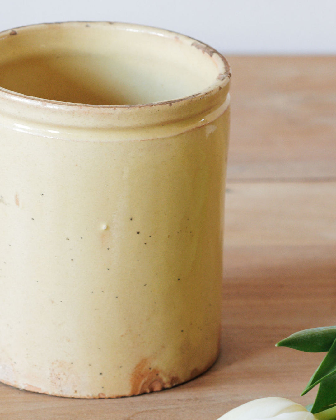 A distressed pale yellow ceramic pot sits on a wooden surface.