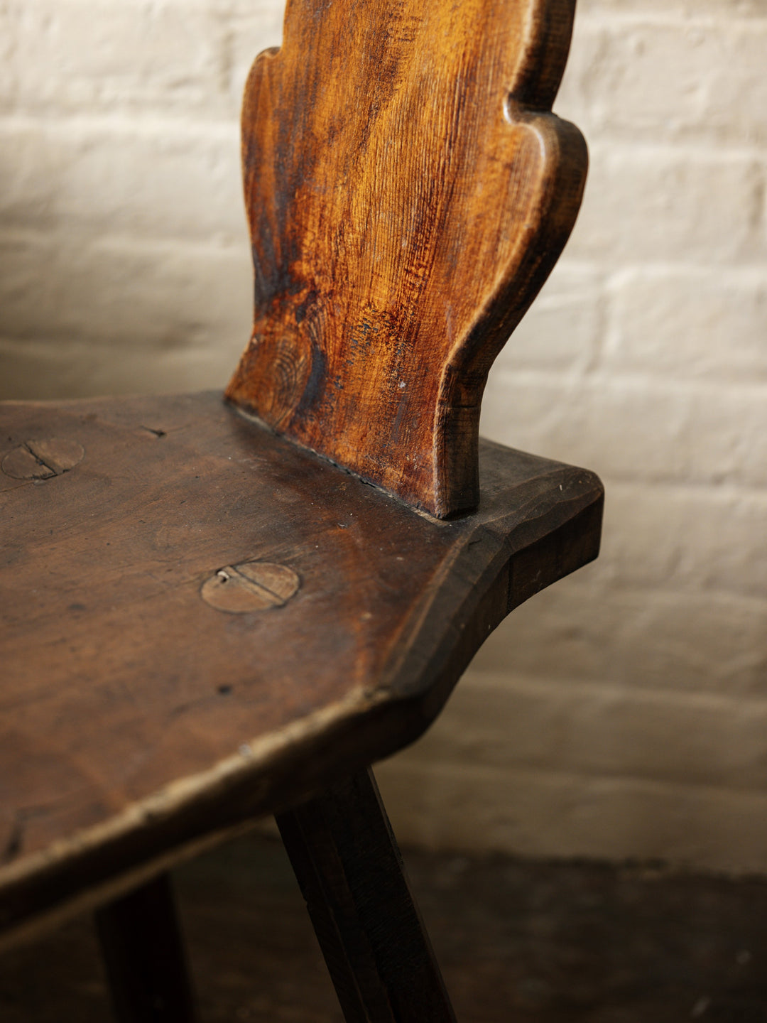 a close up of a wooden chair against a white brick wall