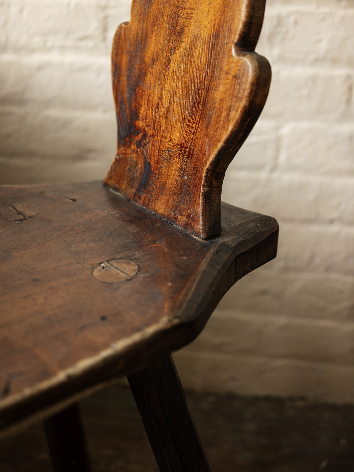 a close up of a wooden chair against a white brick wall