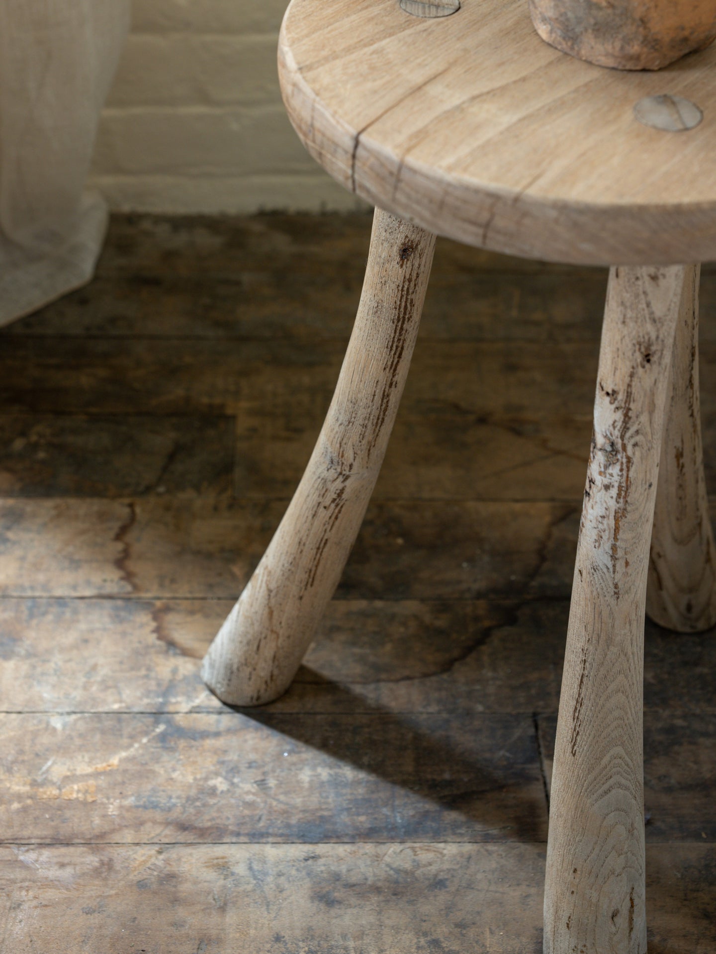 le curved leg tripod stool is sitting on a wooden floor .