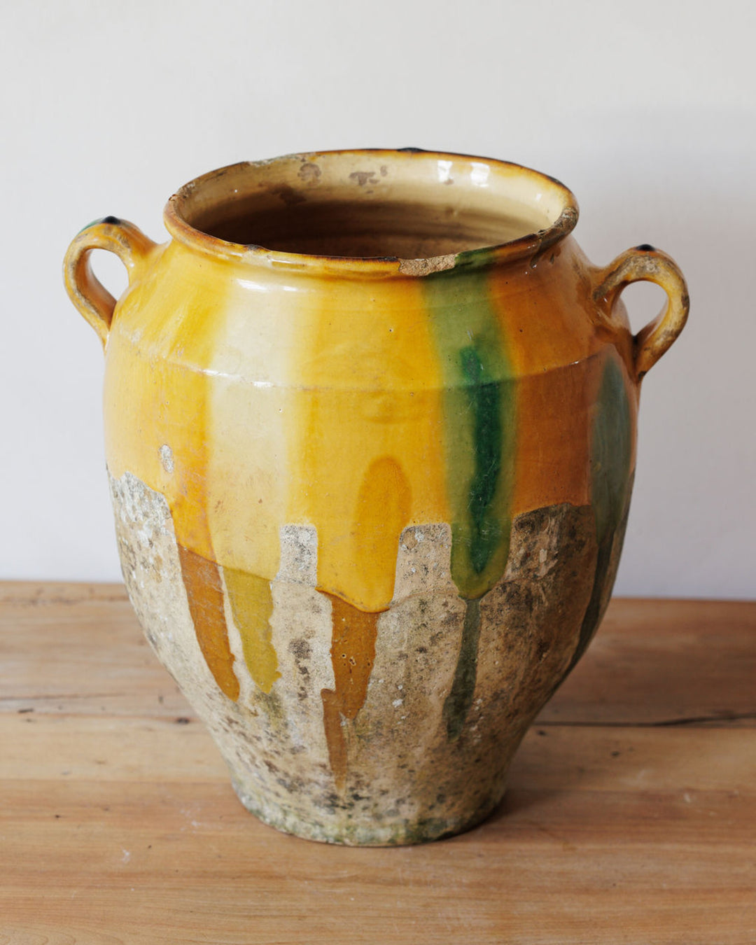 Antique two-handled ceramic pot with dripping yellow and green glaze over a weathered, unglazed base.