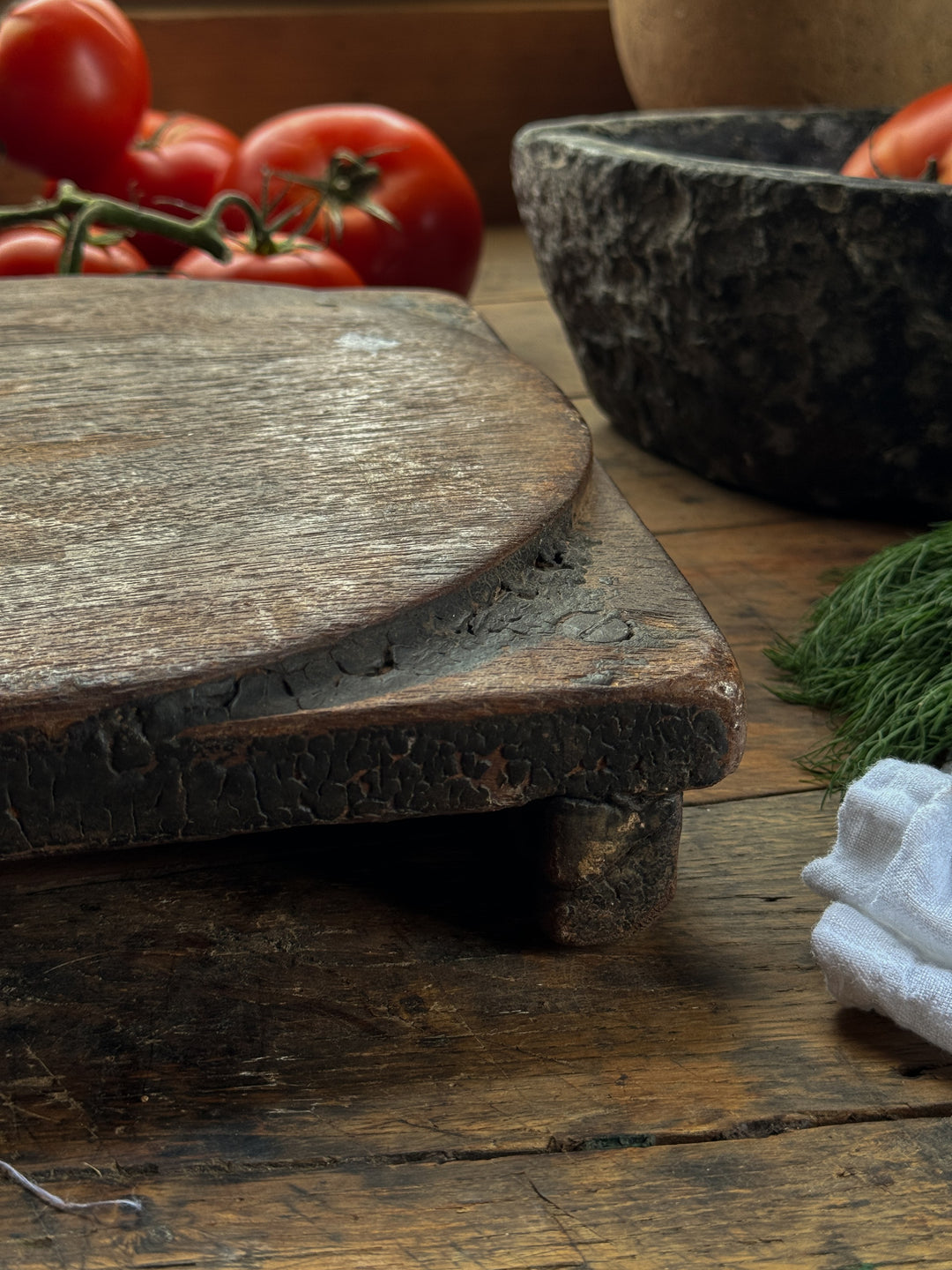 a wooden cutting board with tomatoes and dill on a wooden table .
