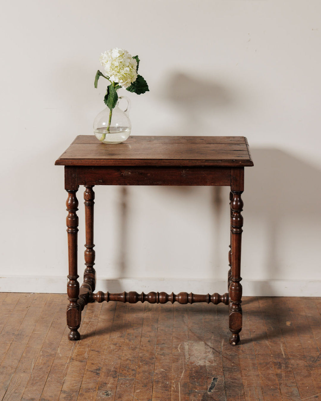 A rustic wooden table with a white hydrangea in a glass vase.