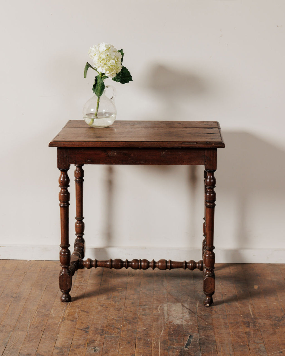 A rustic wooden table with a white hydrangea in a glass vase.