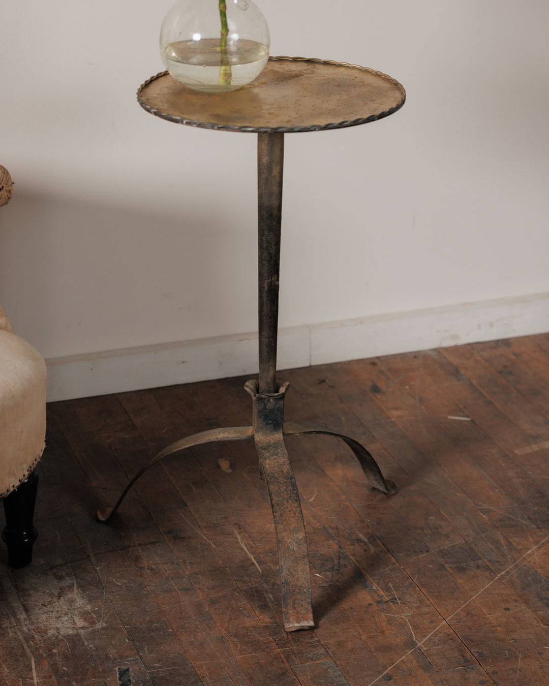 A dark metal pedestal table with a round top and a three-legged base, holding a glass vase with a plant.