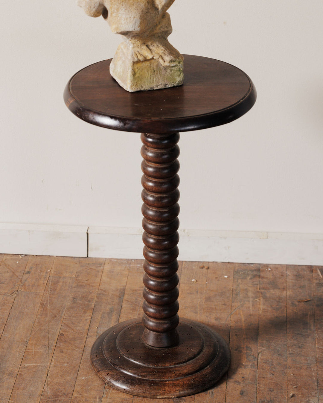 Dark wood pedestal table with a spiraled column, topped by a light-colored stone sculpture.