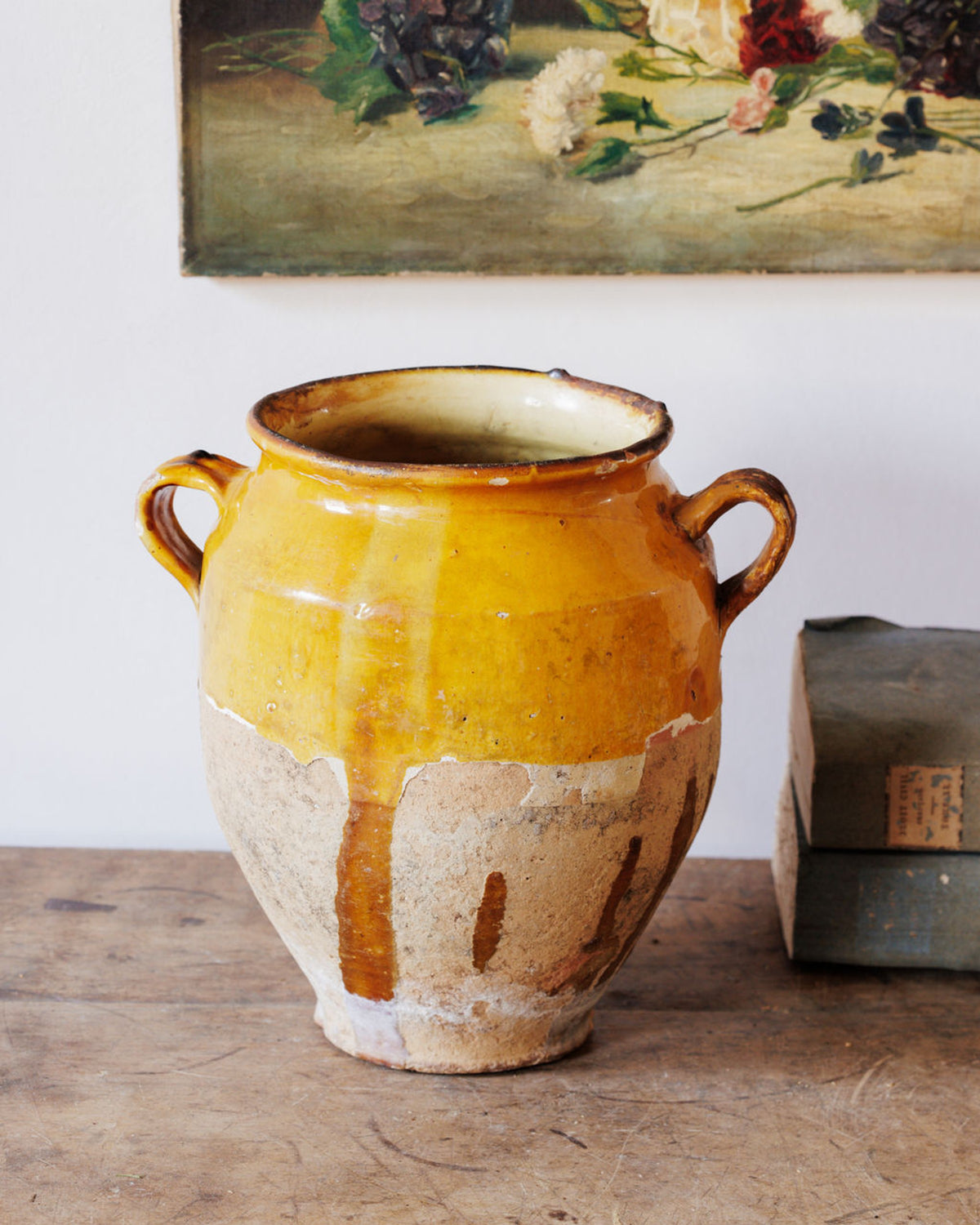 Rustic two-handled terracotta pot with yellow glaze dripping onto its unglazed base, on a wooden table.