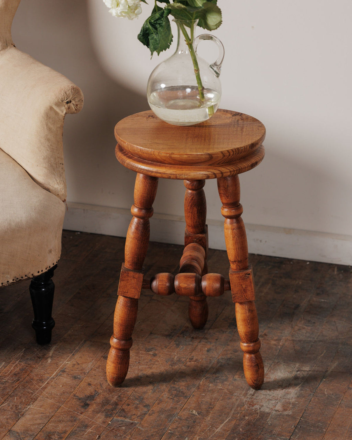 A wooden stool with a vase holding a plant stem, next to an armchair.