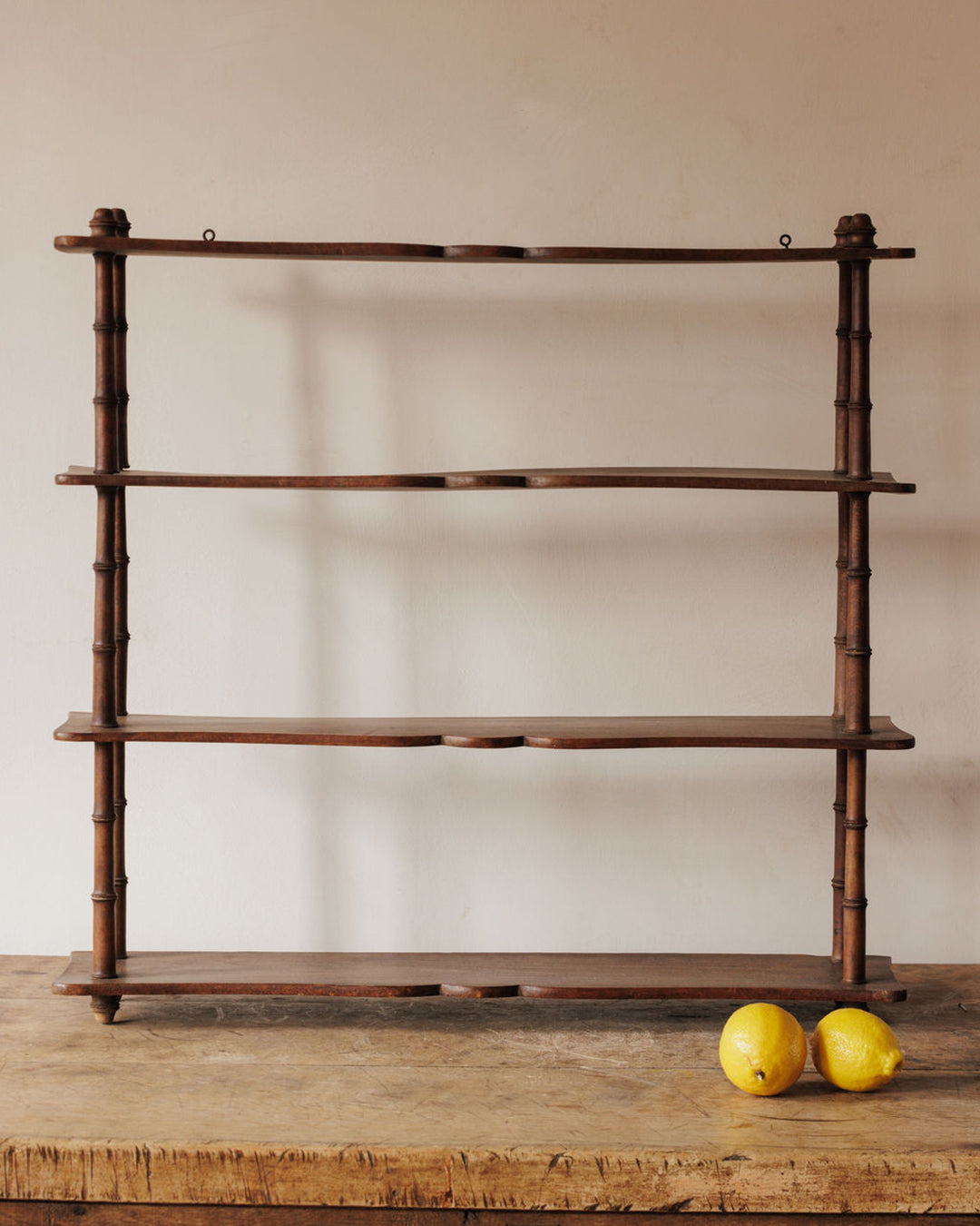 Dark wood 4-tier shelf with bamboo-style supports on a wooden table, with two lemons.