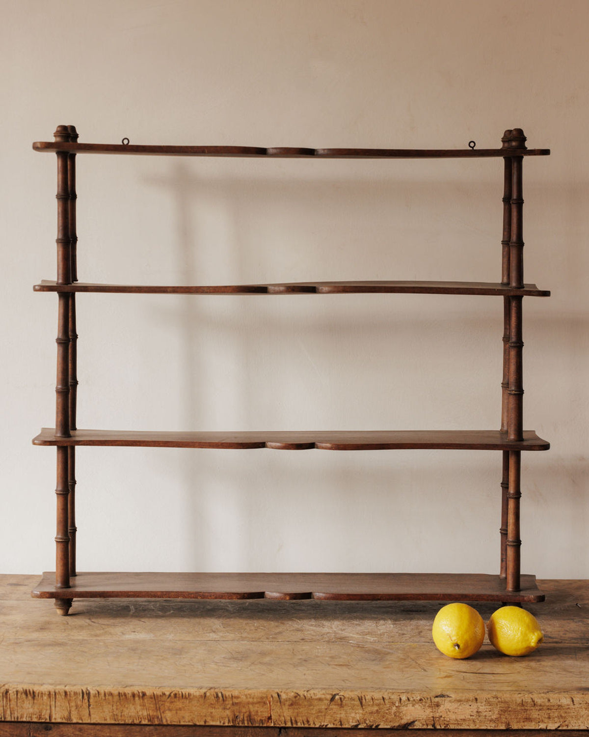 Dark wood 4-tier shelf with bamboo-style supports on a wooden table, with two lemons.