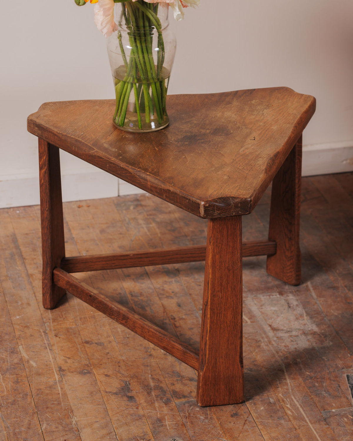 Rustic three-legged triangular wooden stool with a vase of flowers.