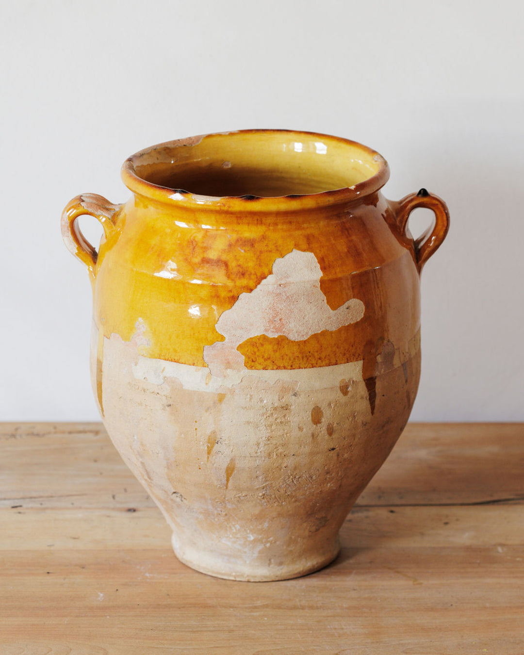 Rustic pottery pot with two handles, yellow glaze, and exposed terracotta.