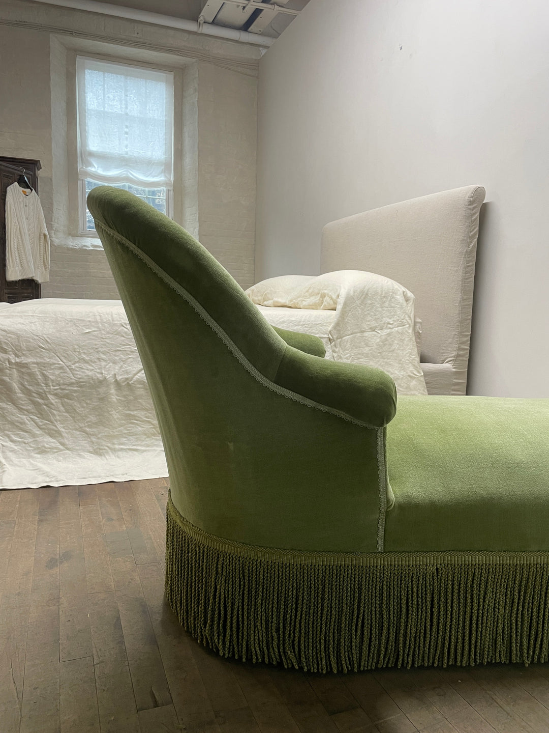 a green chaise lounge with fringe is in a bedroom next to a bed .