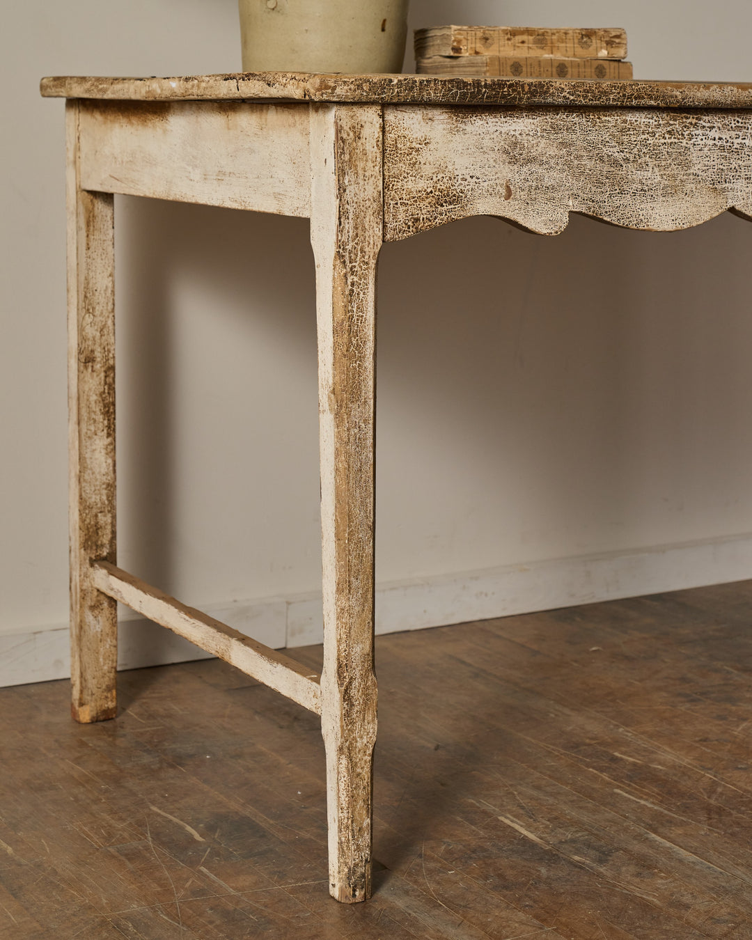 Antique white wooden table with flaking paint, a scalloped apron, and a lower stretcher.