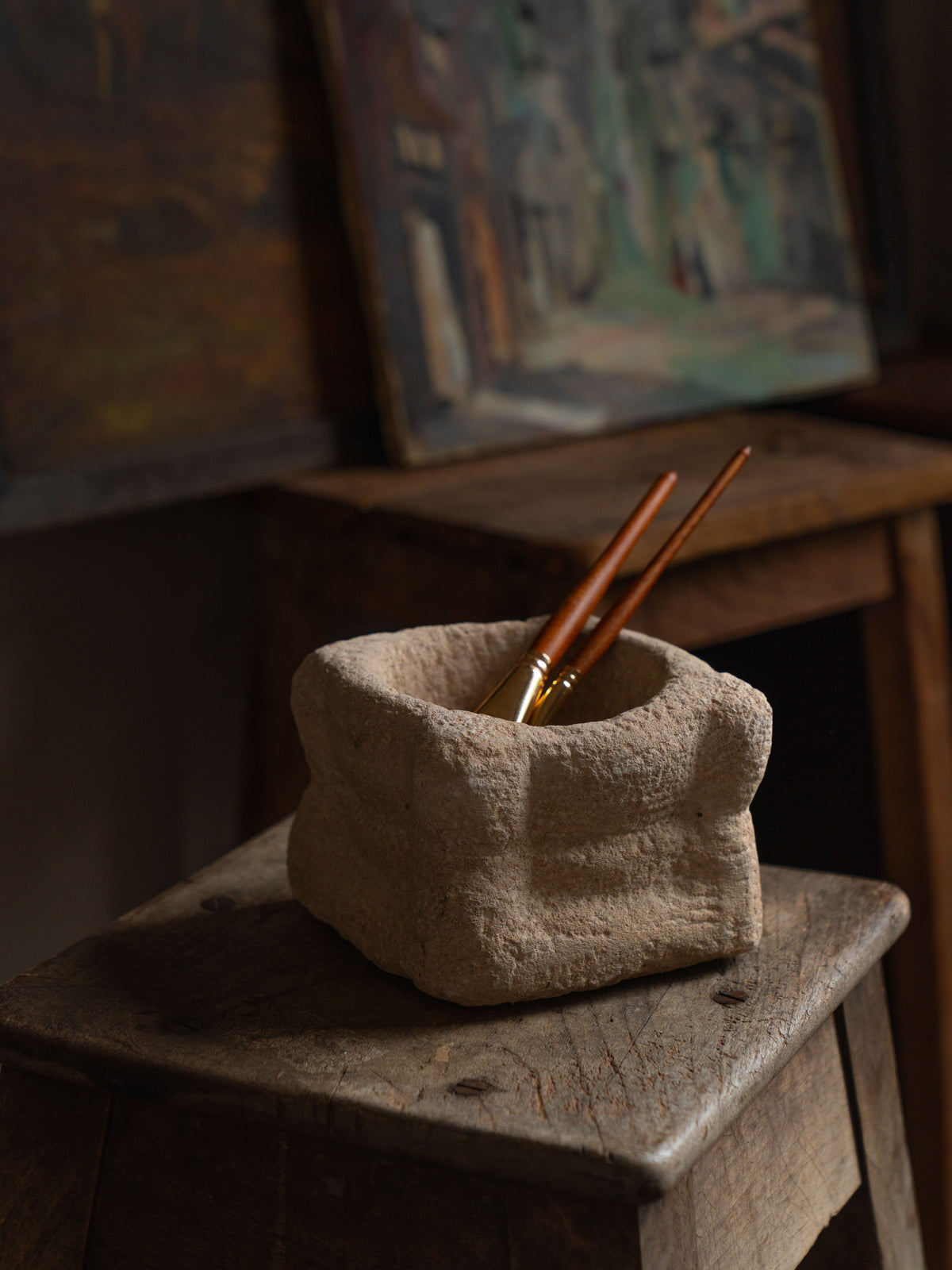 two brushes are in a stone container on a wooden stool .