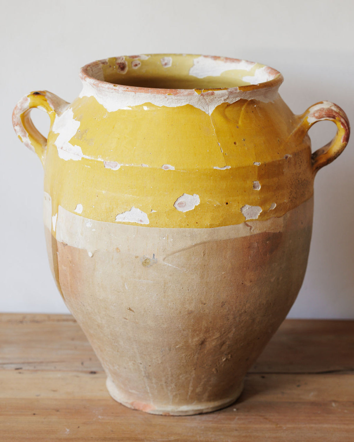 Two-handled ceramic pot with peeling yellow glaze over an unglazed clay base.