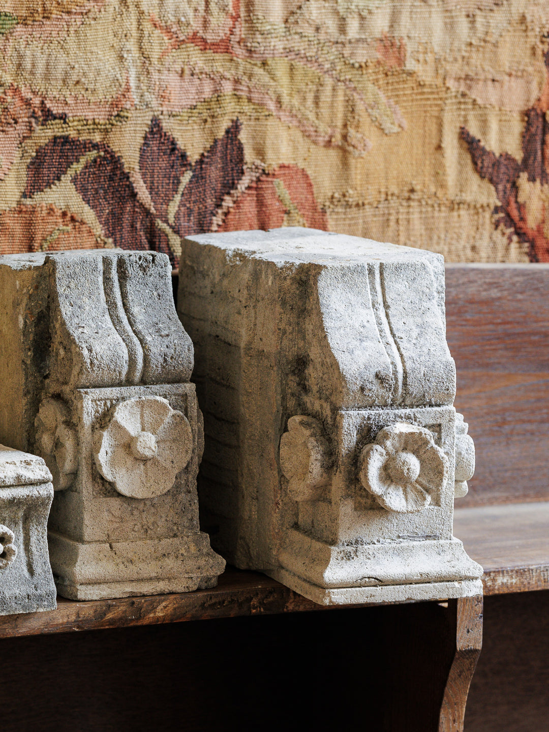two stone sculptures are sitting on a wooden shelf in front of a tapestry .