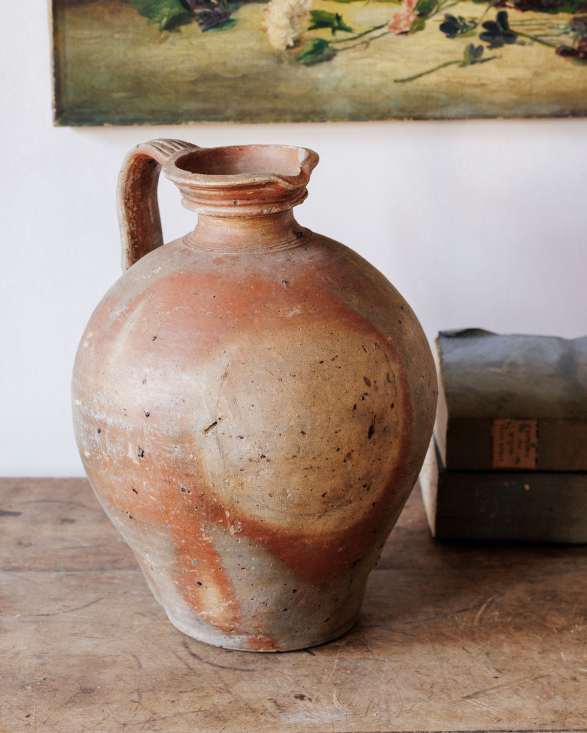 An aged earthenware pitcher with a chipped rim and mottled reddish-brown and beige surface on a wooden table.