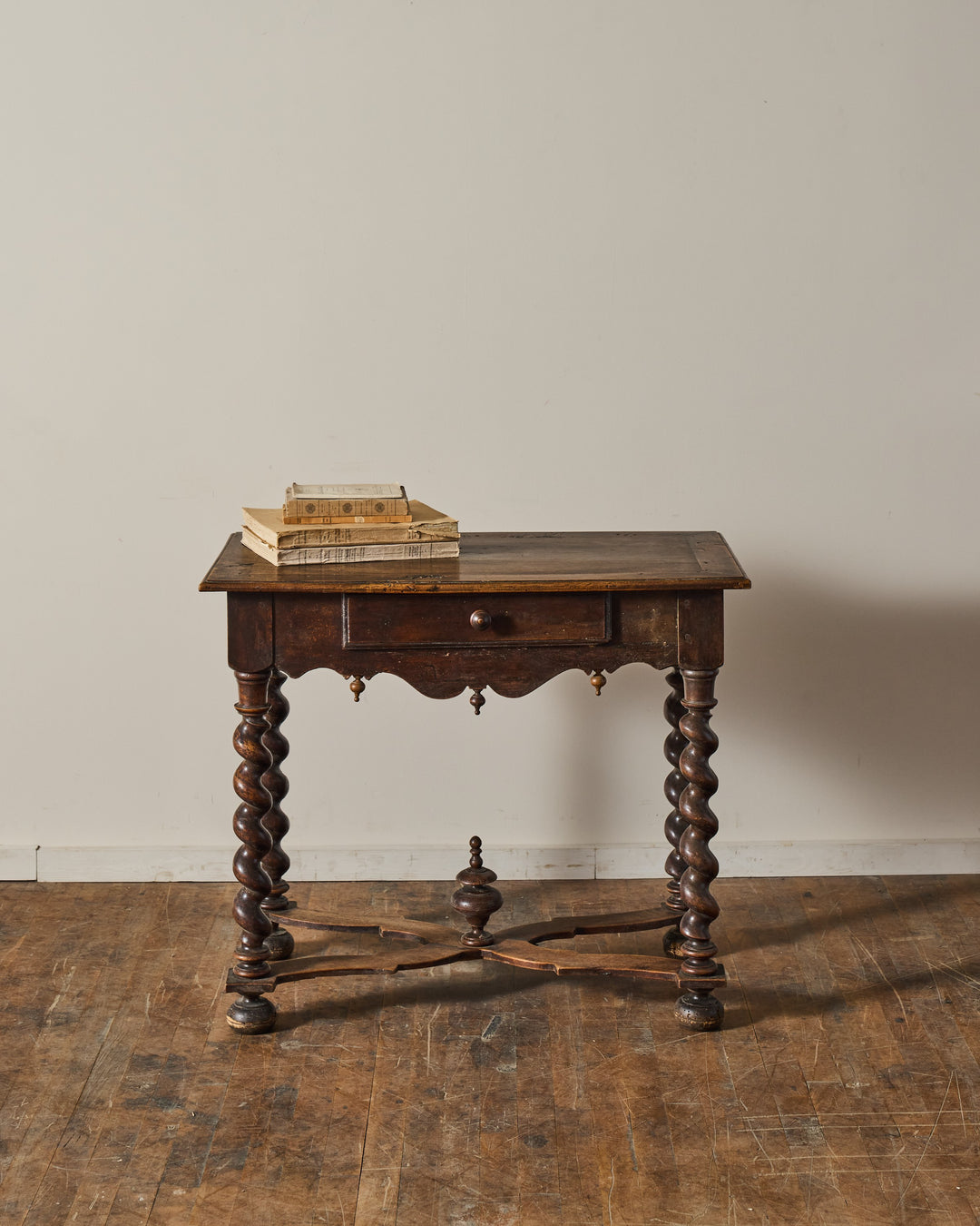 Antique dark wood table with barley-twist legs, a single drawer, and old books stacked on top.