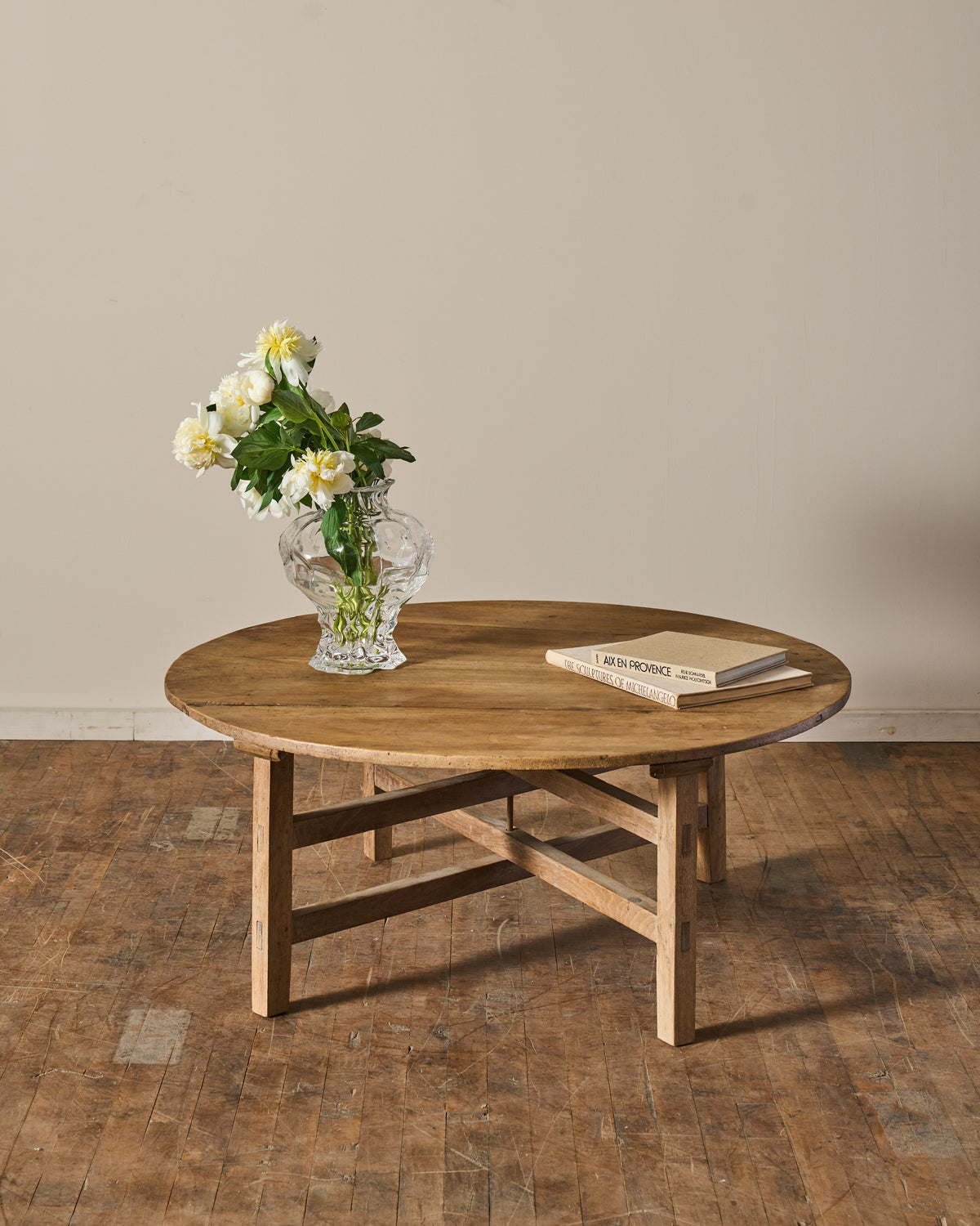 Rustic round wooden coffee table with a vase of white flowers and a book, on a wooden floor.