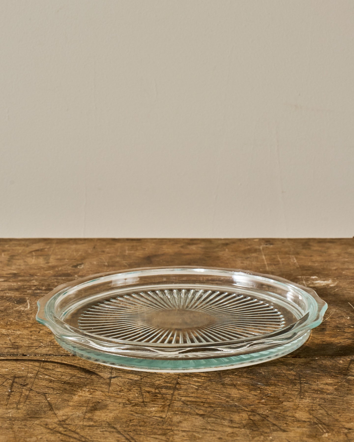 Clear glass pie plate with a ribbed sunburst pattern on a wooden surface.
