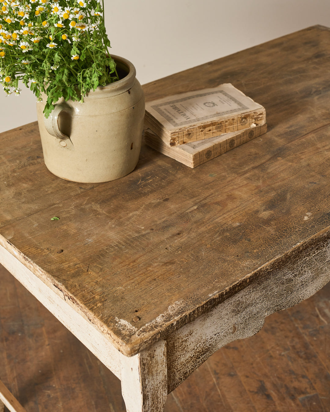 A rustic distressed wooden table holds a pot of chamomile flowers and old books.