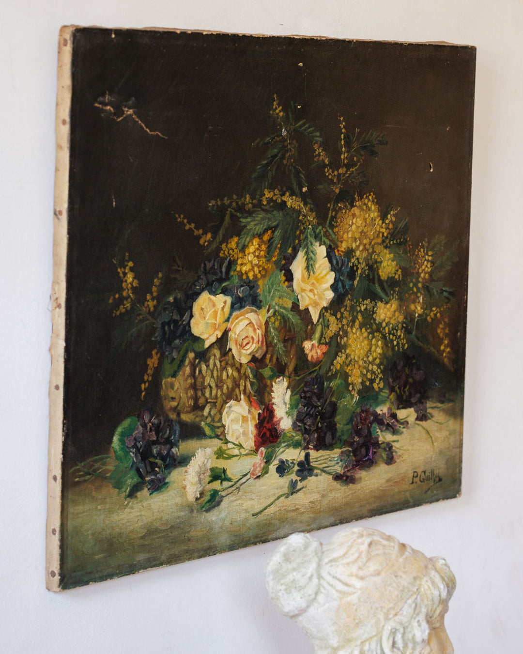Oil painting still life of yellow mimosa, light roses, and dark grapes on a light surface with a dark background.