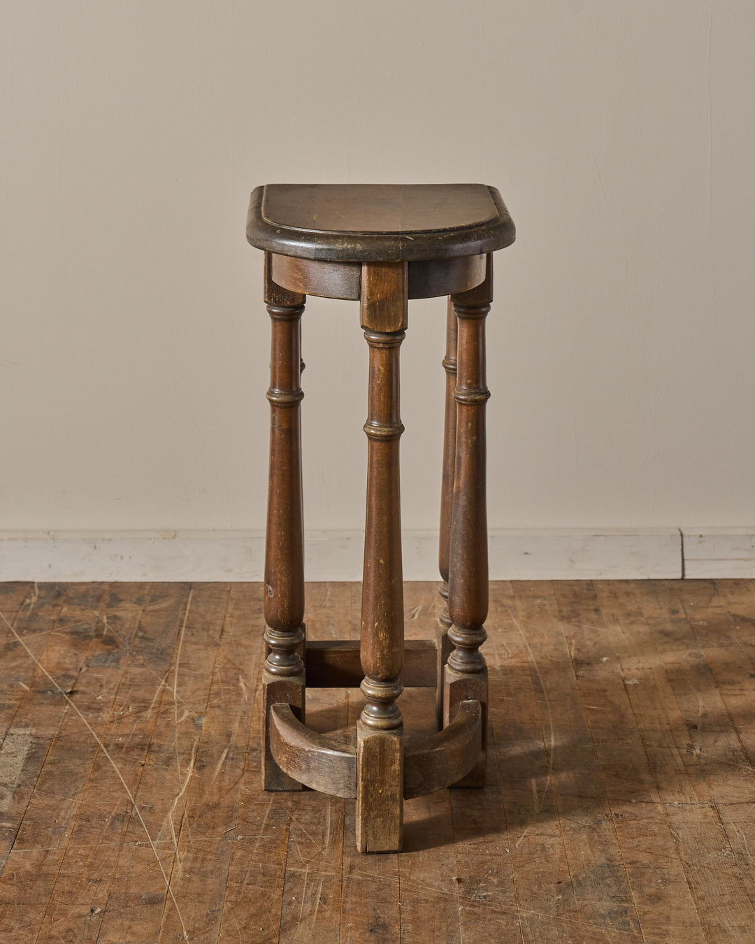A vintage wooden pedestal with a semi-circular top and turned legs.