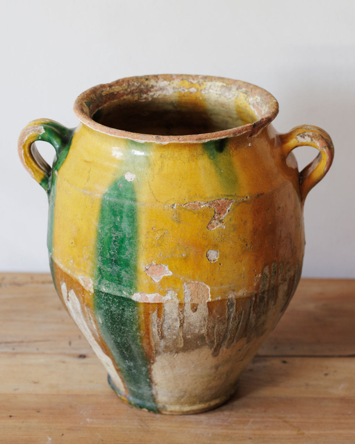 Rustic yellow and green ceramic pot with handles on a wooden surface.
