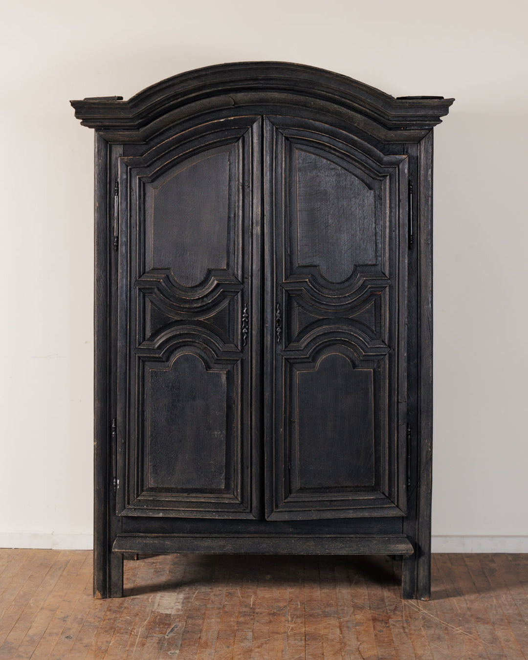 Dark distressed wooden armoire with carved panel doors and an arched top.