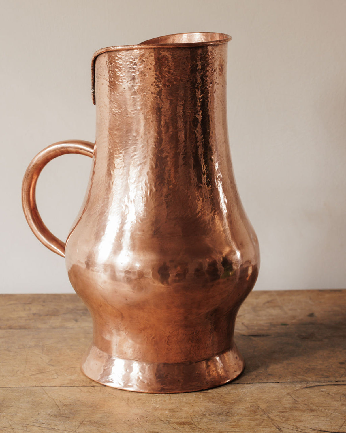 A hammered copper pitcher on a wooden table.