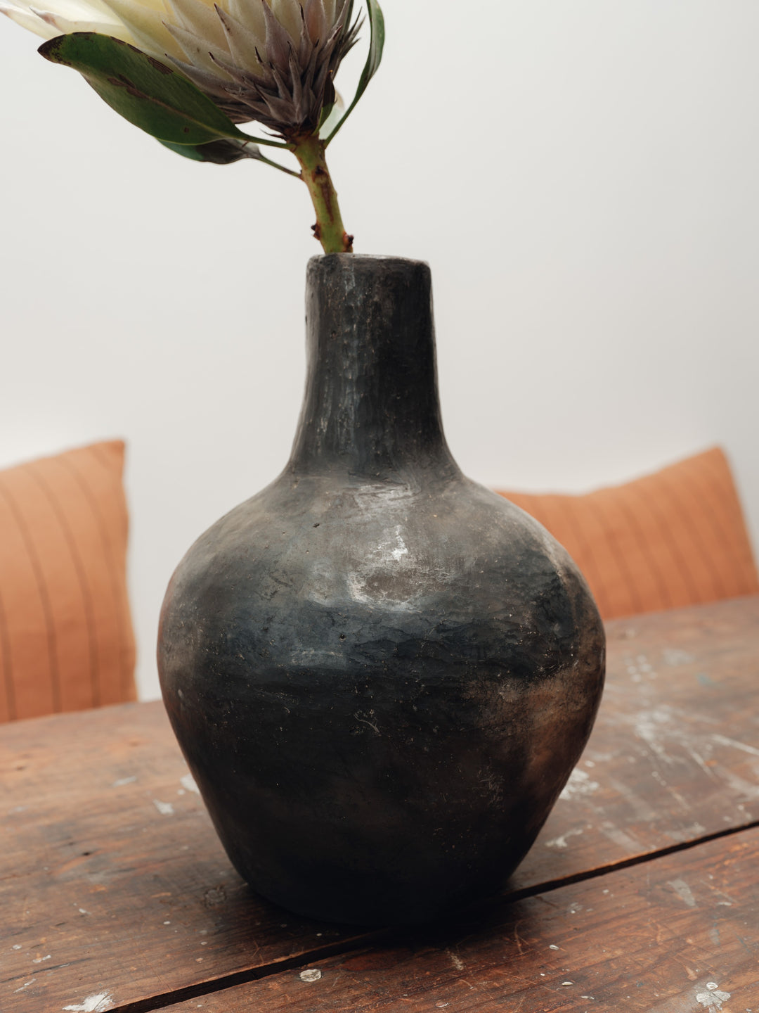 a black vase with a flower in it sits on a wooden table