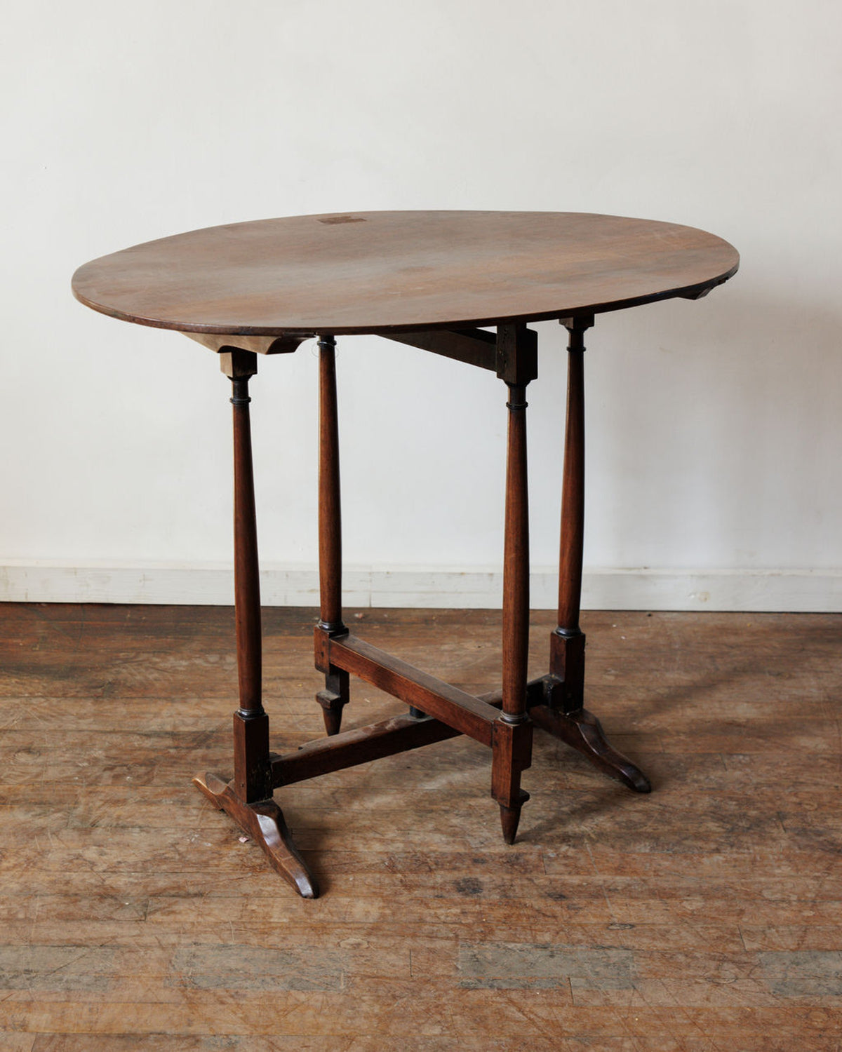 An antique oval drop-leaf wooden table with turned legs.