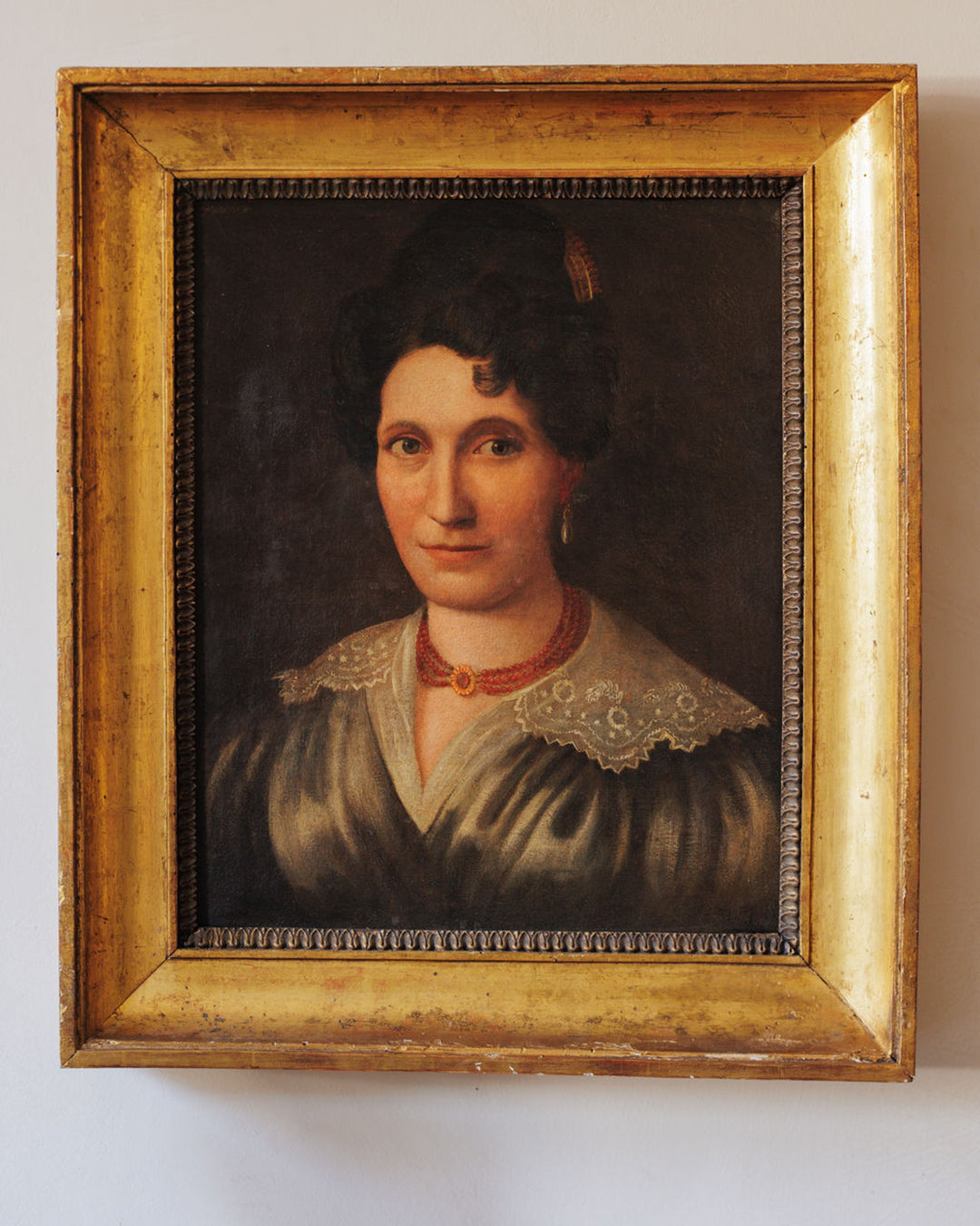Framed oil portrait of a woman with dark hair, wearing a white lace collar and a red beaded necklace.