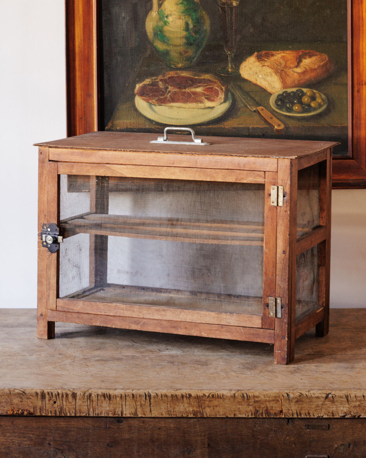 Rustic wooden food safe with mesh doors and shelves, on a wooden counter.