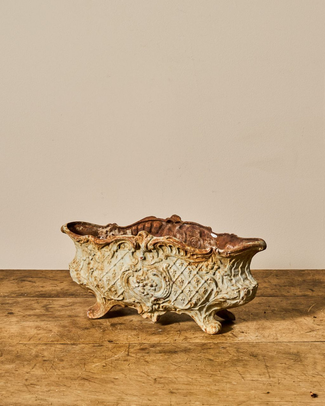 Weathered, ornate rectangular cast iron planter with scrollwork on a wooden surface.