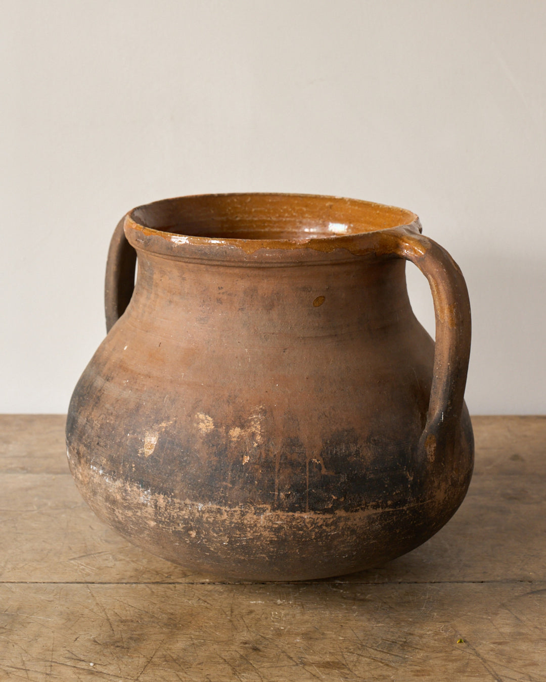 Rustic earthenware pot with two handles, a glazed rim, and a dark, worn base.