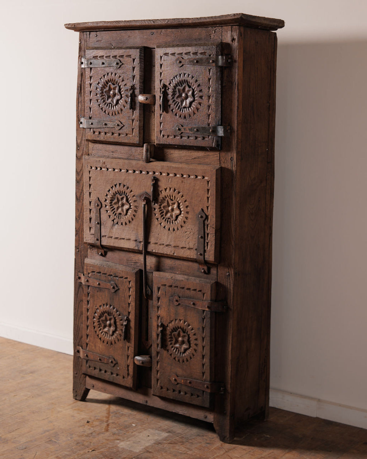A rustic wooden cabinet with six doors, each featuring carved star motifs and ornate metal hardware.