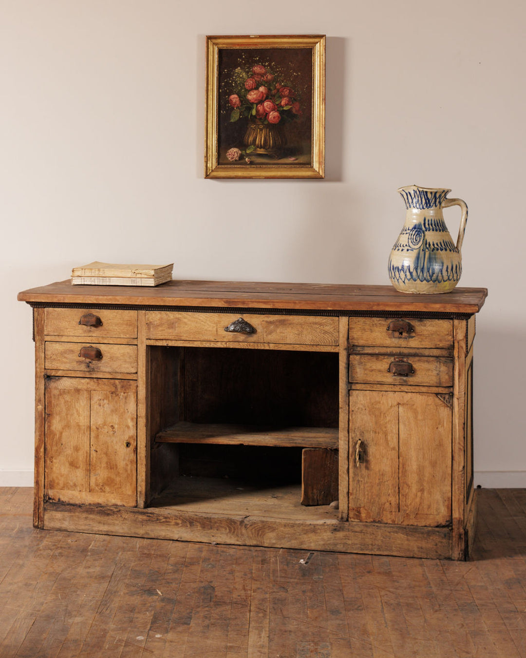 Rustic wooden cabinet with a still life painting of roses, books, and a blue and white jug.