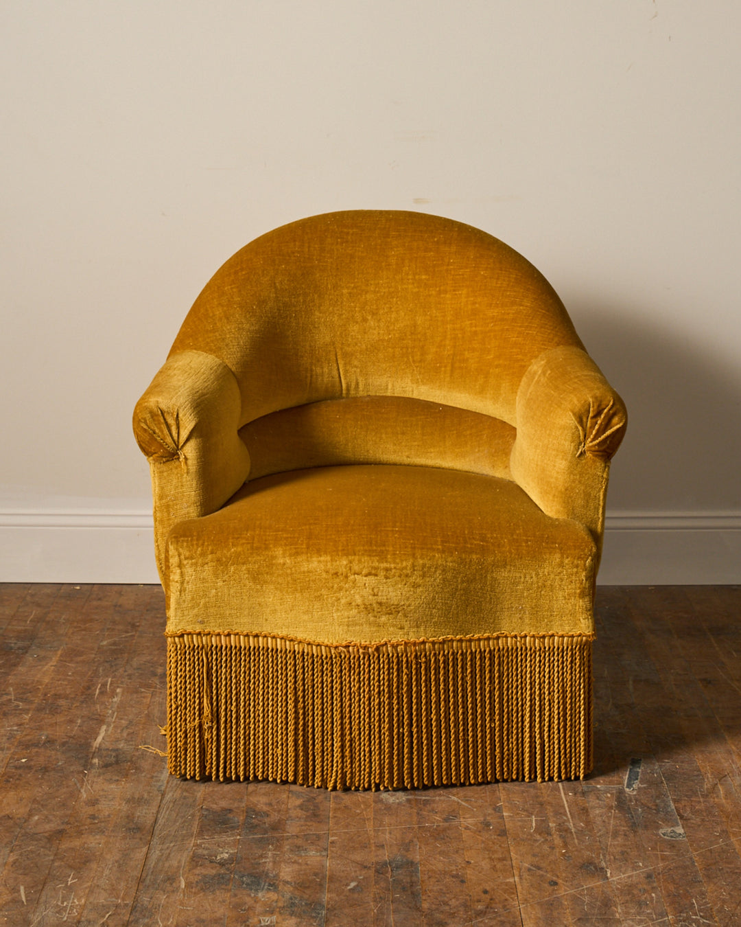 A mustard yellow velvet armchair with fringe trim.