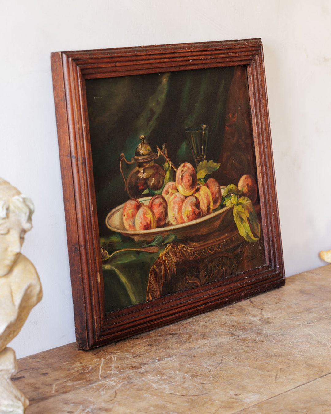 Still-life painting of peaches, a teapot, and a glass in a dark wooden frame.