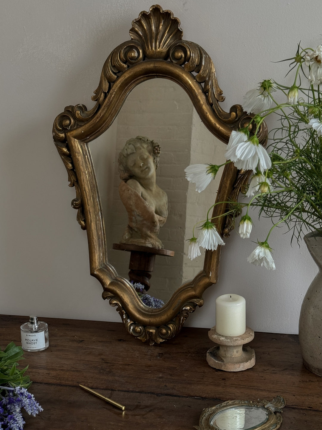 a table with a mirror a vase of flowers and a candle