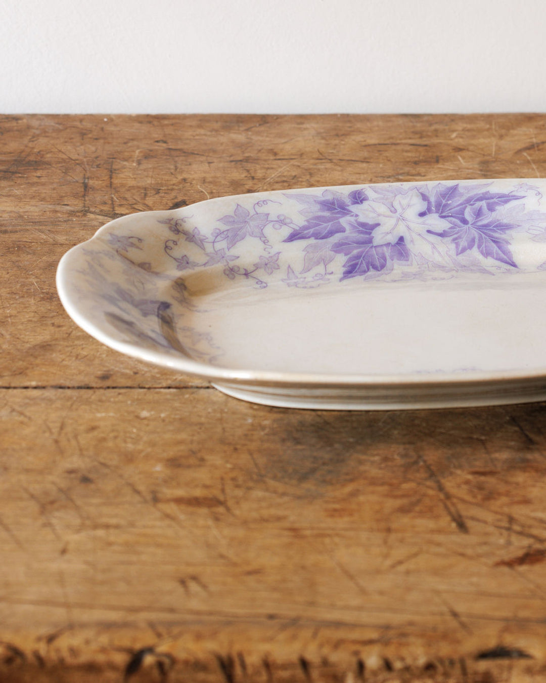 Oblong white serving dish with purple ivy leaf decoration on a wooden table.