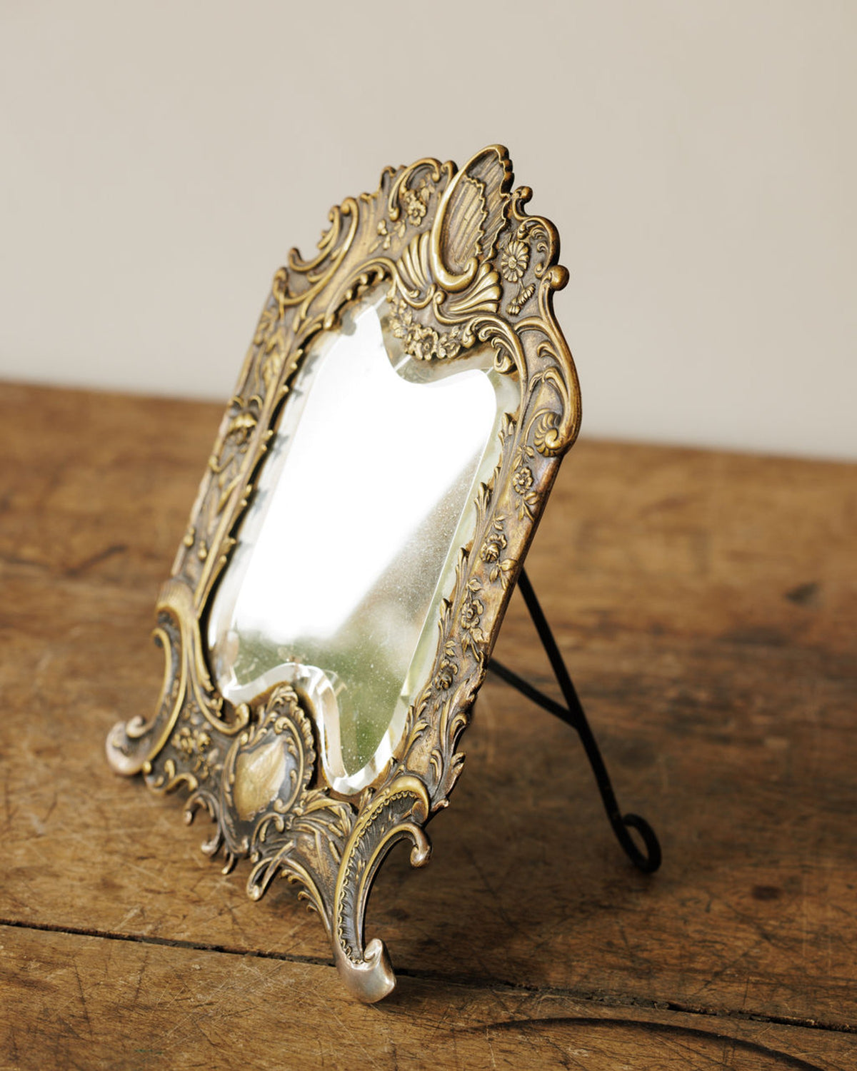 Ornate brass-toned antique standing mirror on a rustic wooden table.